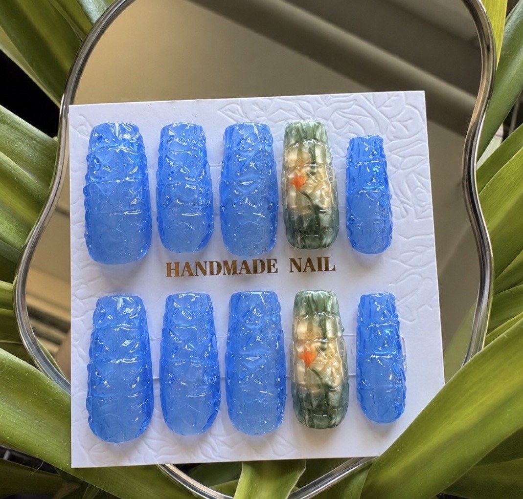 Blue textured press-on nails with green floral accent nails