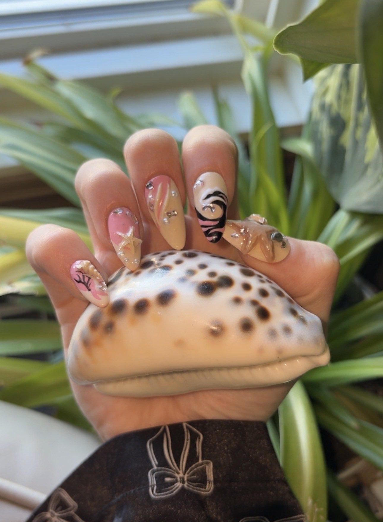 Ocean-inspired almond nails with starfish, gems and pink and black accents